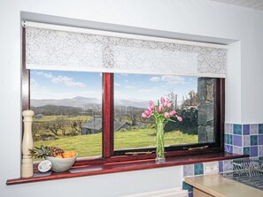 Una cocina con ventana, un frutero y un jarrón con flores.