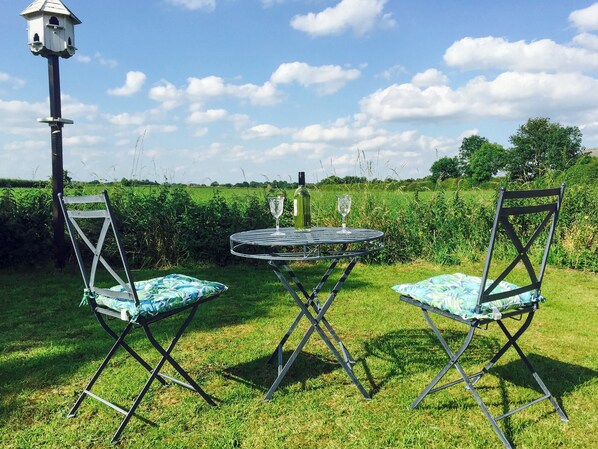 Un área de estar al aire libre con dos sillas y una mesa, un comedero para pájaros y un campo de césped al fondo.