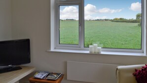 A room with a large window, a flat-screen TV, a small table with magazines, and a radiator. - 2 bedroom accommodation in Caythorpe, near Nottingham (Caythorpe, near Nottingham)