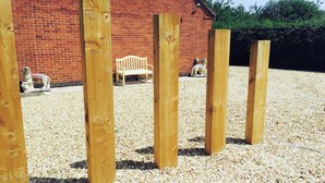 A wooden structure with vertical beams in a gravel area, a brick building, and a bench in the background. - 2 bedroom accommodation in Caythorpe, near Nottingham (Caythorpe, near Nottingham)