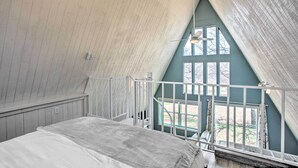 Un dormitorio con techo inclinado, una cama, un ventanal con cortinas y vistas al exterior.