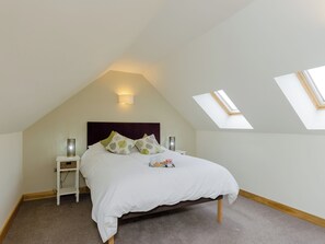 A bedroom with a sloped ceiling, a bed with white bedding, two bedside tables, and a skylight.