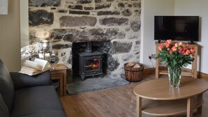 A stone fireplace, a television, a sofa, a table, and a vase with flowers. - 3 bedroom accommodation in Kyle of Lochalsh (Kyle of Lochalsh)