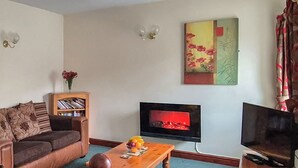 Una sala de estar con un sofá, una mesa de centro con fruta, un televisor de pantalla plana, una estantería y un cuadro en la pared.
