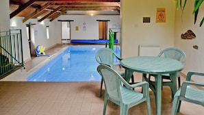 Una piscina interior con techo de madera, una mesa con sillas y un letrero de precaución en la pared.