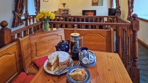 Un área de comedor con una mesa de madera dispuesta para el té, un jarrón con flores amarillas y una estantería de fondo.