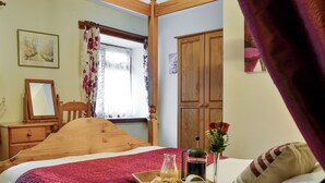 Un dormitorio con cama y cómoda de madera, un espejo, una ventana con cortinas de encaje y un armario de madera.