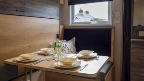 Un área de comedor con una mesa dispuesta para dos personas, una ventana con vistas a edificios y un cabecero tapizado oscuro.