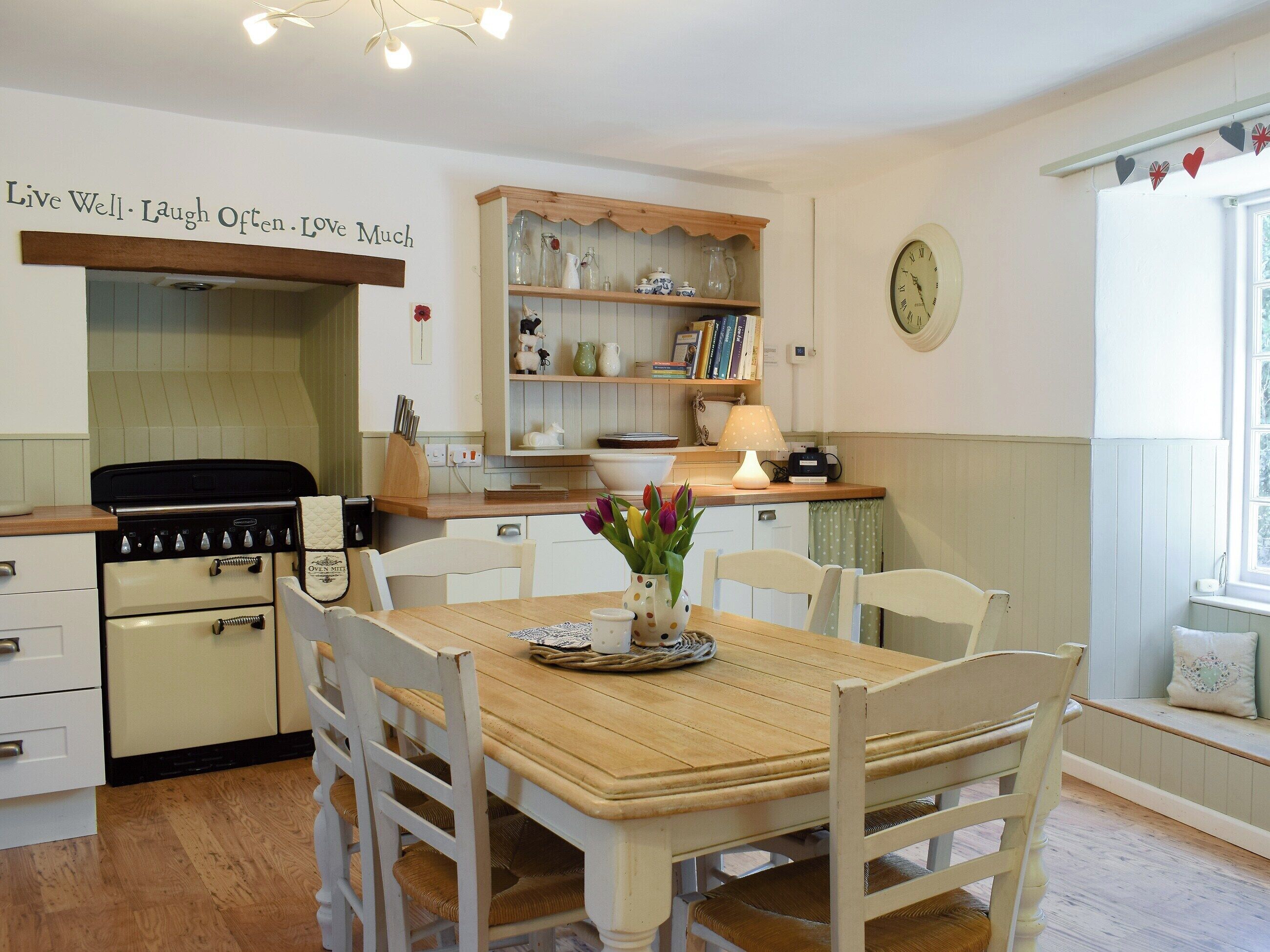 Una cocina acogedora con una mesa de madera, sillas blancas, una estufa y estantes con utensilios de cocina.