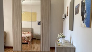 A hotel room with a large mirror, a wooden dresser, a bed with floral bedding, and a patterned floor. - Casa Antonia-in a strategic area to visit the main attractions of Naples (Piazza-Tralia-Pendolo)