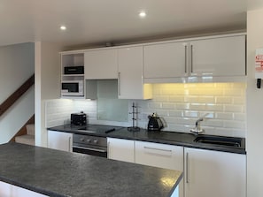 A modern kitchen with white cabinets, a black countertop, a microwave, a toaster, a kettle, and a sink.