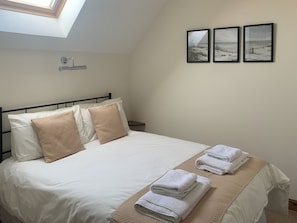 A neatly made bed with pillows, a bedside table, and a wall-mounted towel rack with towels.