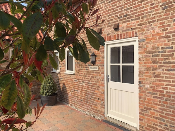 A brick building with a white door, a potted plant, and a sign that reads 'MILLHOUSE'.