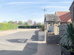 A paved driveway leading to a wooden structure with a tiled roof, a brick wall, and a metal fence.