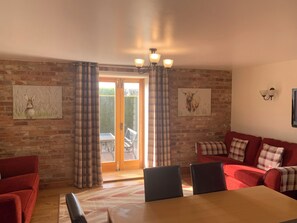A cozy room with a brick wall, a wooden table, red sofas, and two paintings.