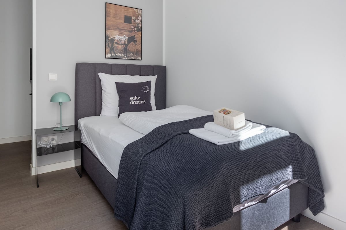Une chambre à coucher moderne avec un lit, une table de chevet avec une lampe, un tableau accroché au mur et un luminaire au plafond.