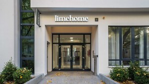 L'entrée de Limehome se distingue par ses portes en verre, un chemin d'accès dégagé et un panneau indiquant le numéro « 4 » au-dessus.