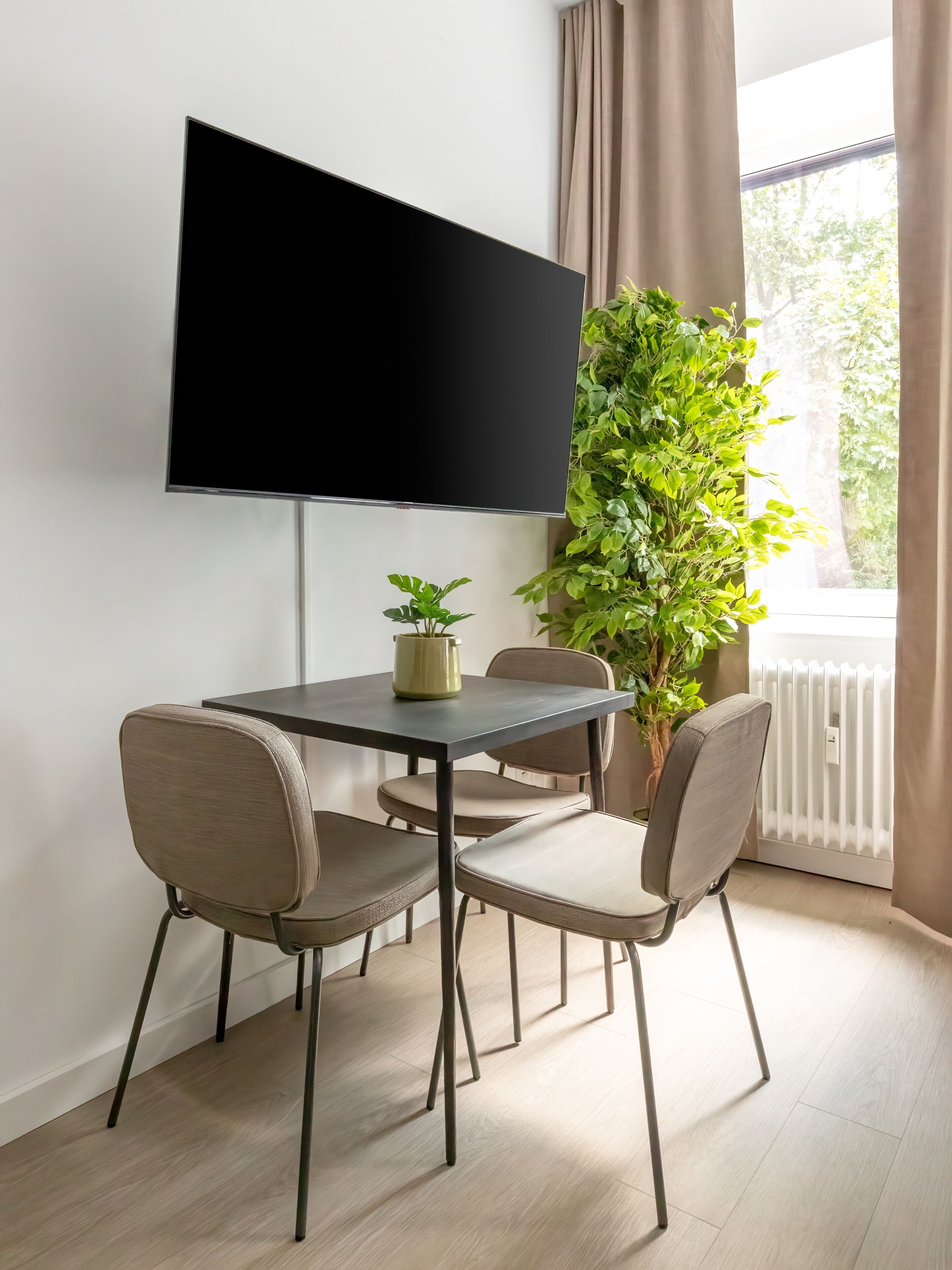 Een moderne eetruimte met een tafel, stoelen, een potplant en een flatscreen televisie aan de muur.