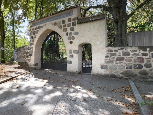 A stone archway with a metal gate, surrounded by trees and a stone wall. - Limehome Berlin Luise-Henriette-Str. (Berlin)