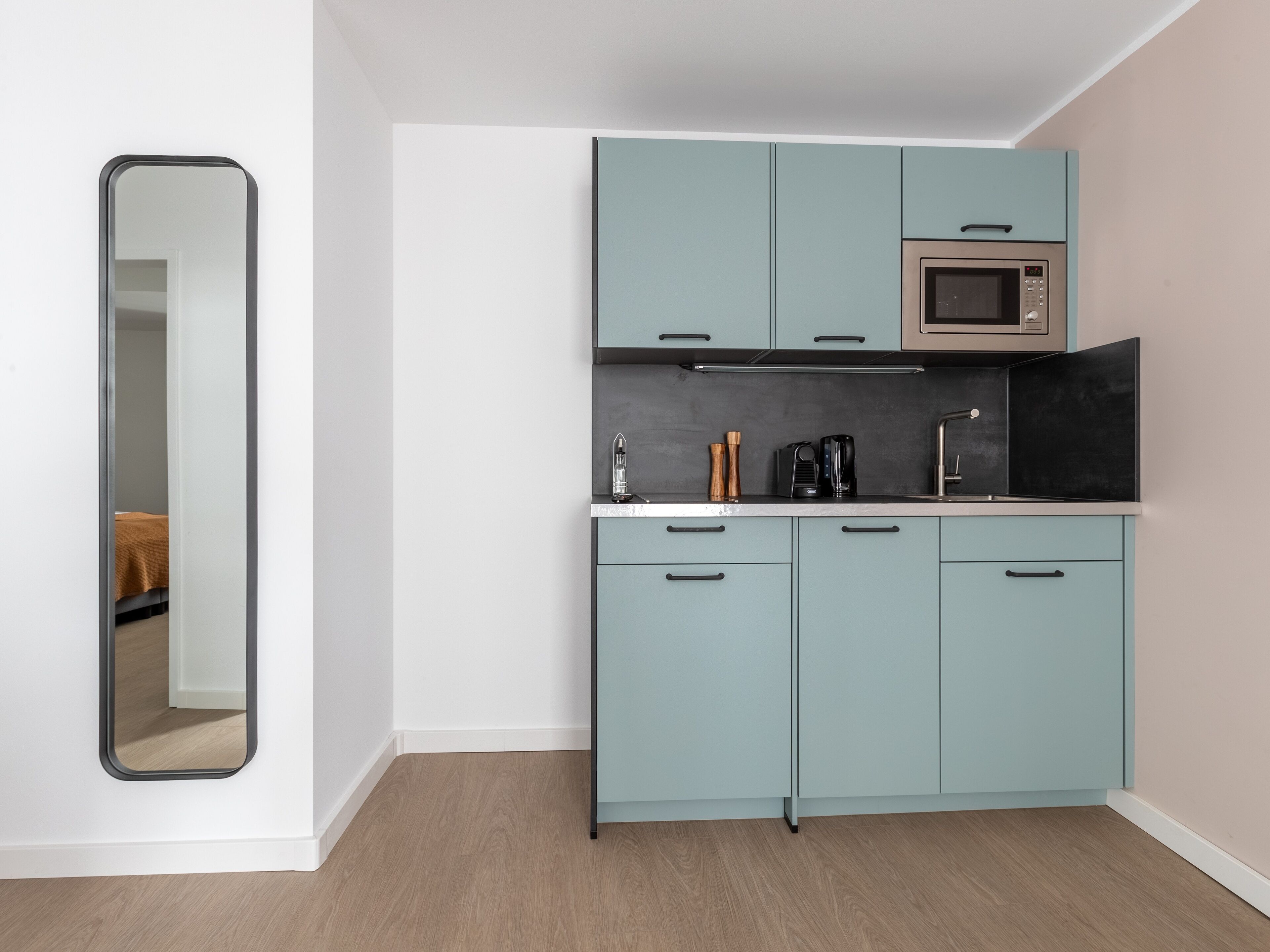 A compact kitchen with teal cabinets, a microwave, and a coffee maker.