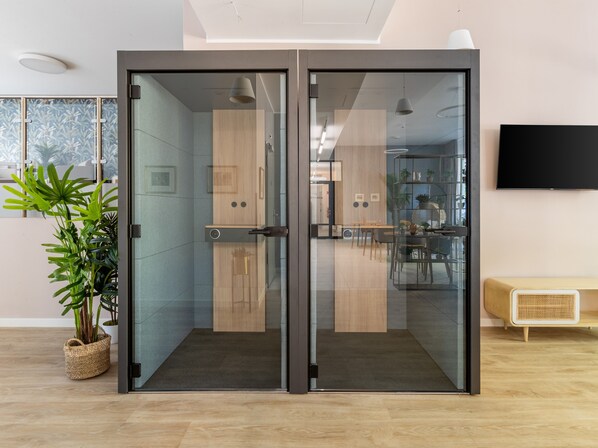 Un interior moderno con un puerta corrediza de vidrio que da a un comedor, un televisor de pantalla plana montado en la pared y una planta en maceta en el suelo.