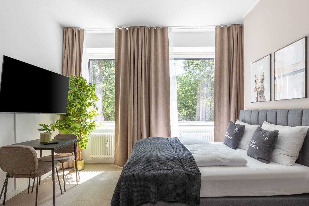 Une chambre d’hôtel moderne équipée d’un lit, d’un bureau, d’une télévision et d’une grande fenêtre avec des rideaux.