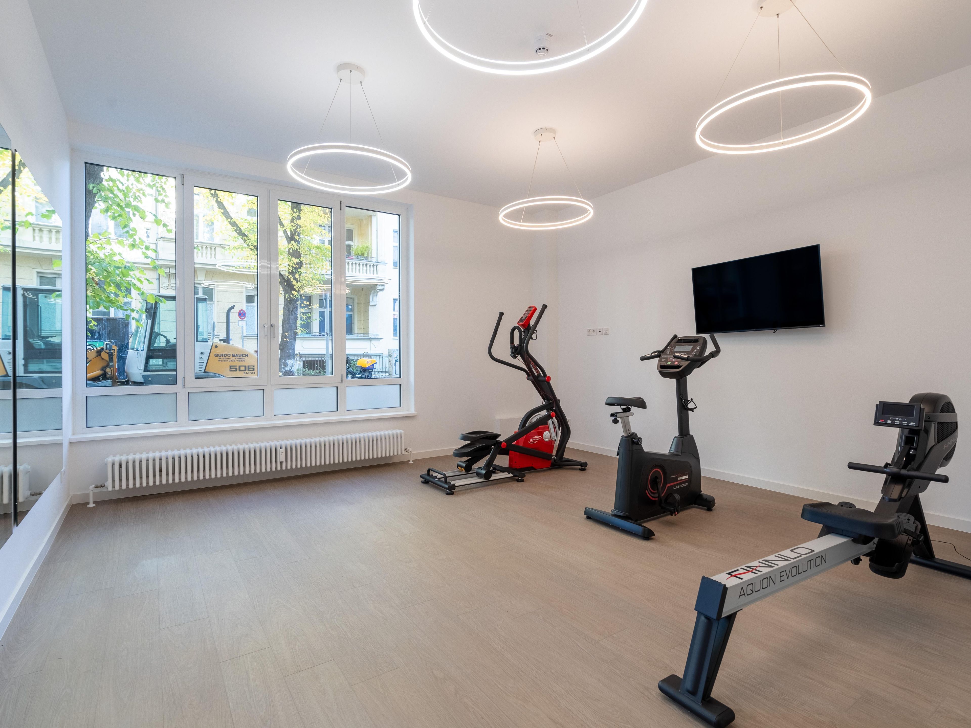 Ett gym med träningsutrustning, stora fönster och en TV som är monterad på väggen.