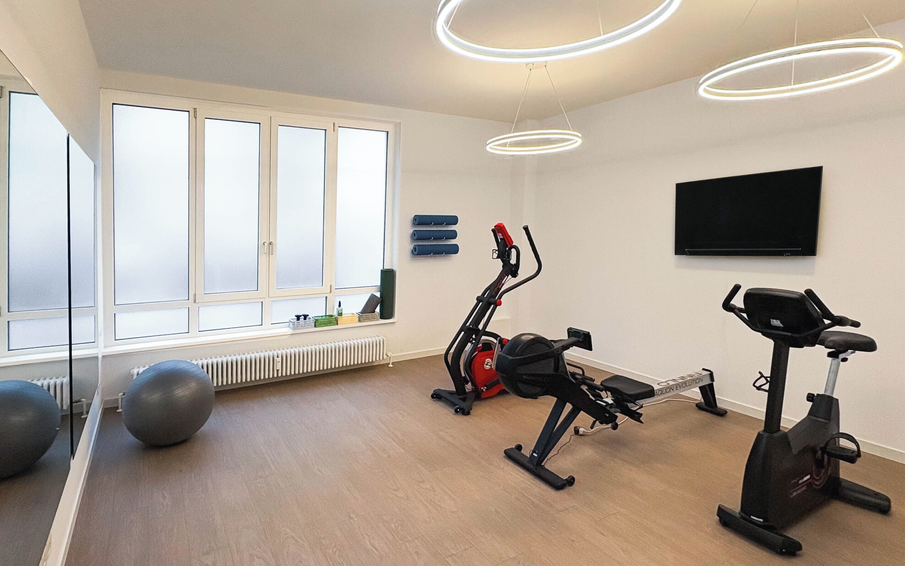 Une salle de sport équipée de matériel d’exercice, dotée de grandes fenêtres et d’un téléviseur à écran plat.