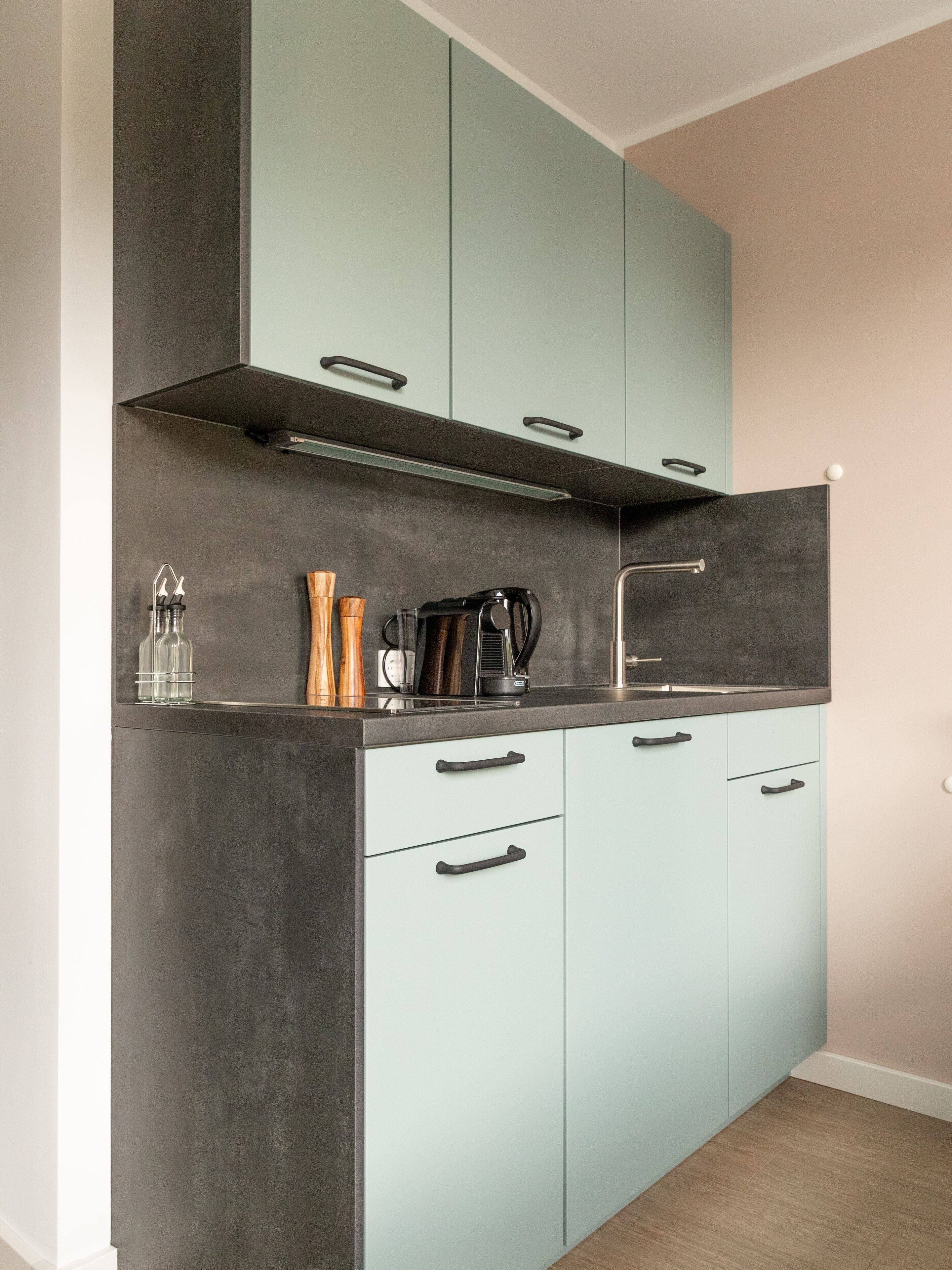 A modern kitchen with light blue cabinets, a dark countertop, and a stainless steel sink.