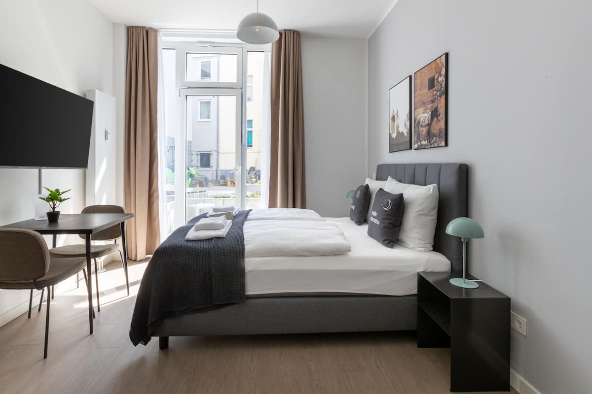 Une chambre d’hôtel moderne, équipée d’un lit, d’une table de chevet, d’une lampe et offrant une vue sur l’extérieur.