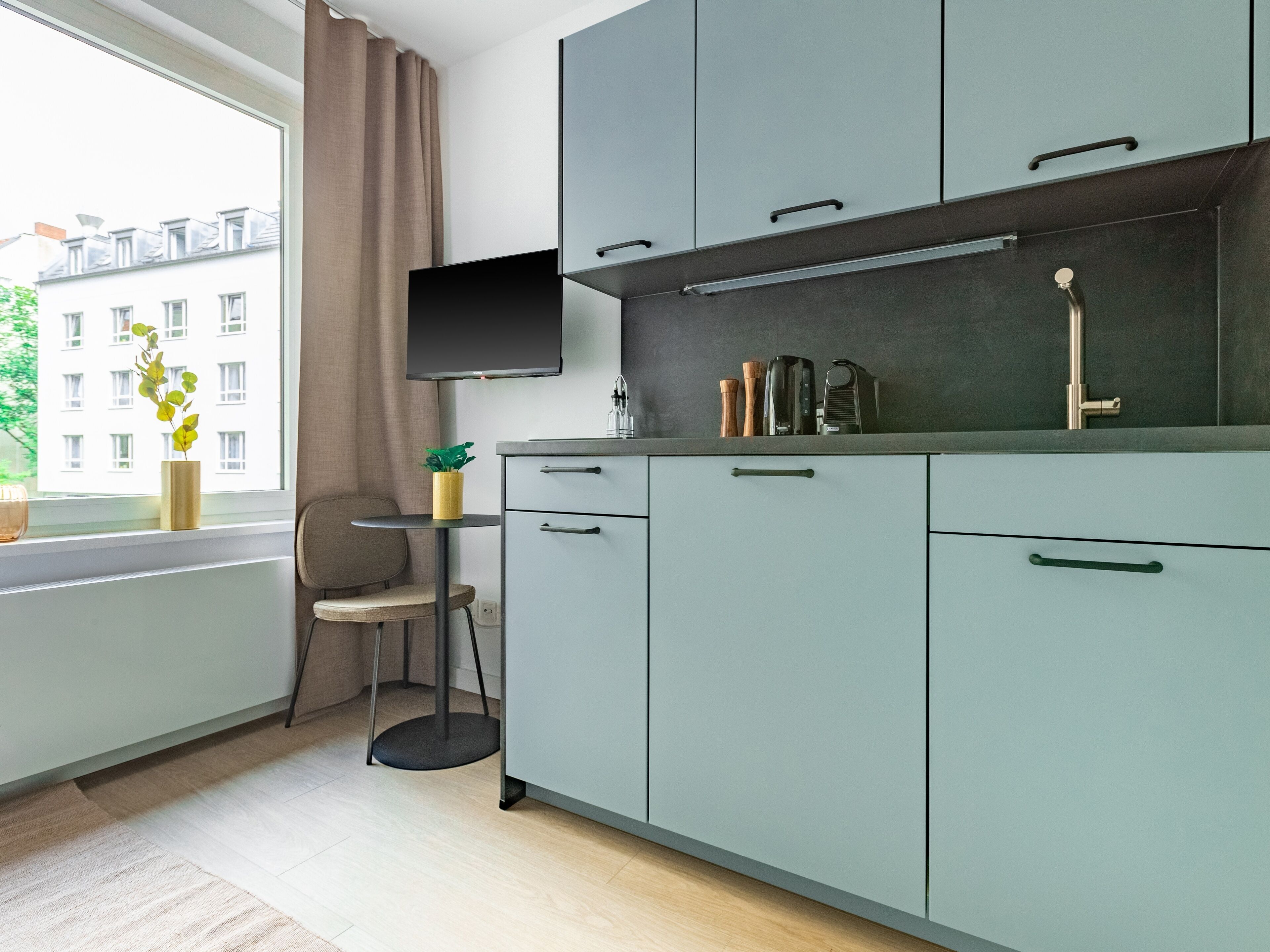 A modern kitchen with grey cabinets, a small round table, a chair, and a window with a view of buildings.