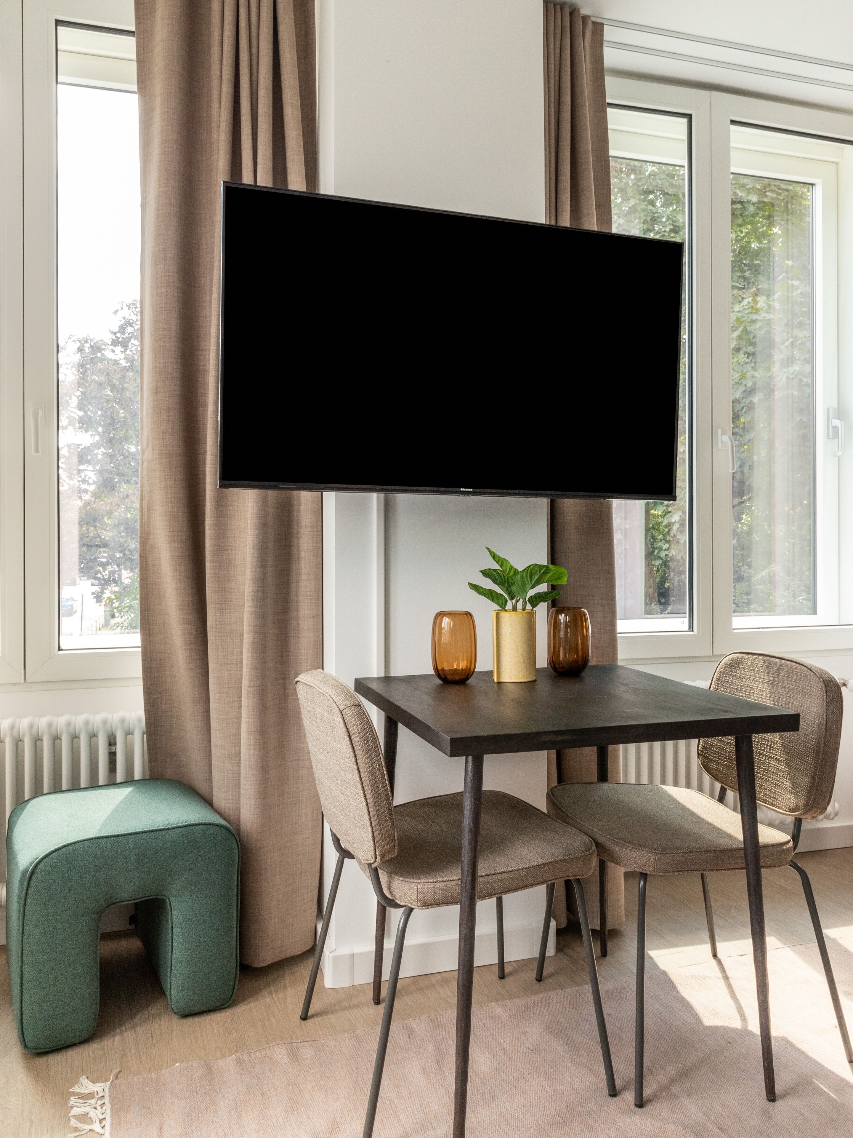 A modern dining area with a large flat-screen TV mounted on the wall, a table with chairs, and a small bench.