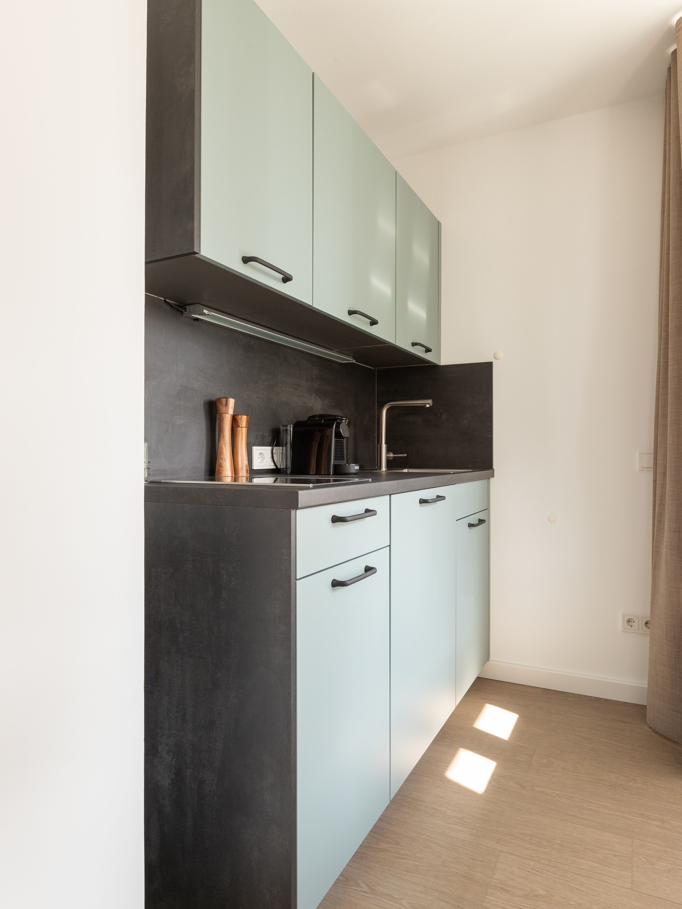 A modern kitchen with light blue cabinets, dark countertops, and a stainless steel faucet.