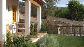 Un patio con mesa y sillas, rodeado de plantas y un muro de piedra.