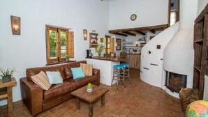 Una sala de estar acogedora con un sofá de cuero marrón, una mesa de centro de madera y una cocina con estufa blanca y vigas de madera.