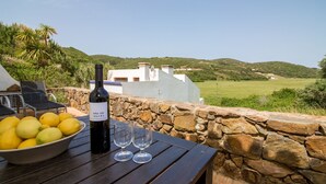 A table with a bottle of wine, glasses, and lemons on a wooden table with a stone wall backdrop. - Casa Verde - sleeps up to 4 (Bordeira)