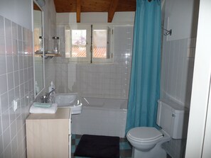 Ein Badezimmer mit Badewanne, Toilette, Waschbecken und einem Fenster mit geöffneten Rollläden.