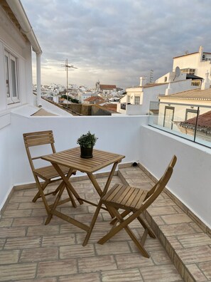 A balcony with a wooden table and chairs, a potted plant, and a view of a cityscape.