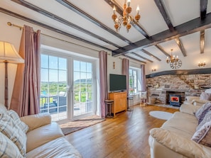 A cozy living room with a stone fireplace, a television, and a balcony with a scenic view.