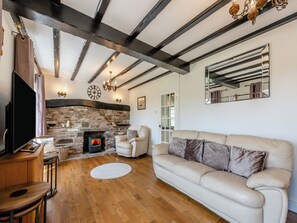 A living room with a stone fireplace, wooden beams, a white sofa, and a television.