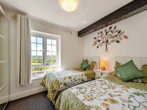 A bedroom with two beds, a window with curtains, a bedside lamp, and a wall decoration.