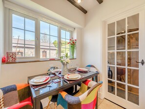 A dining area with a table set for two, a vase with flowers, and a view of the outside through large windows. - 2 bedroom accommodation in Ferryside, near Carmarthen (Ferryside, near Carmarthen)