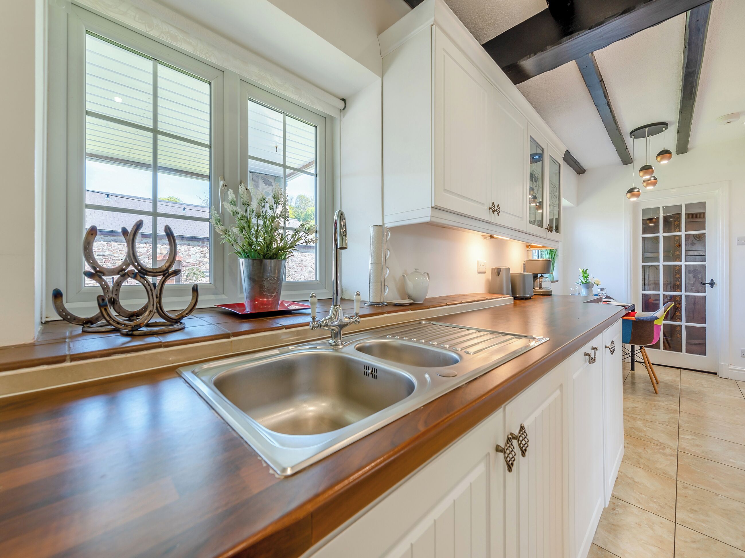 A kitchen with a double sink, white cabinets, a wooden countertop, a potted plant, and a window with blinds.