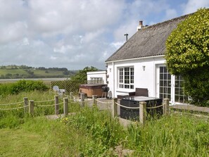 A white building with a black roof, a fenced outdoor area with a barbecue, and a view of the countryside.