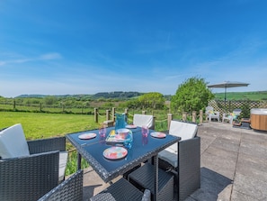 An outdoor patio with a table set for dining, surrounded by wicker chairs and a hot tub. - 2 bedroom accommodation in Ferryside, near Carmarthen (Ferryside, near Carmarthen)