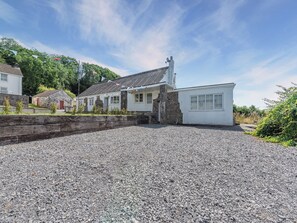 A building with a gravel driveway, stone walls, and a flag. - 2 bedroom accommodation in Ferryside, near Carmarthen (Ferryside, near Carmarthen)