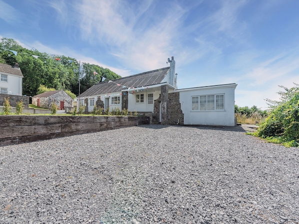 A building with a gravel driveway, stone walls, and a flag. - 2 bedroom accommodation in Ferryside, near Carmarthen (Ferryside, near Carmarthen)