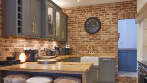 A modern kitchen with a brick wall, dark cabinets, a wooden island with stools, and a large clock.