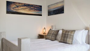 A bedroom with a wooden bed, white bedding, and two paintings on the wall.