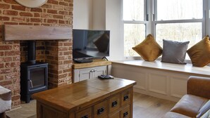 A cozy living room with a brick fireplace, a television, and a window seat with cushions.